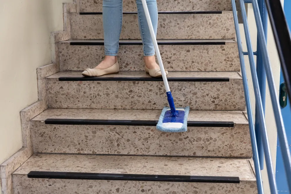 Woman Cleaning Staircase With Dust Mop