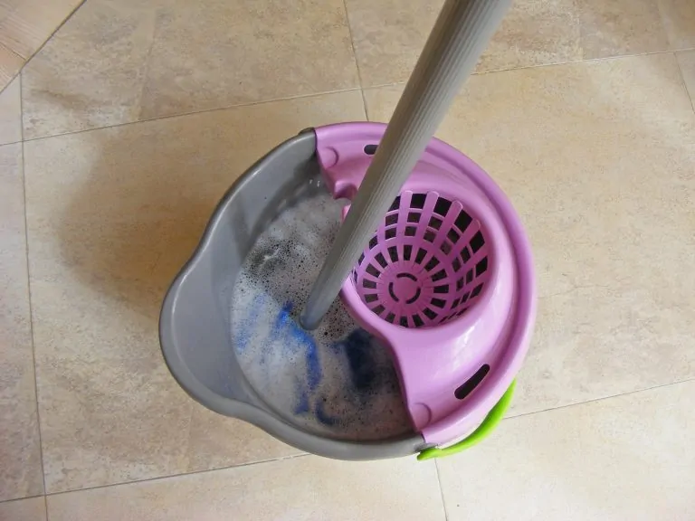 Blue mop inside grey and purple bucket on wet floor