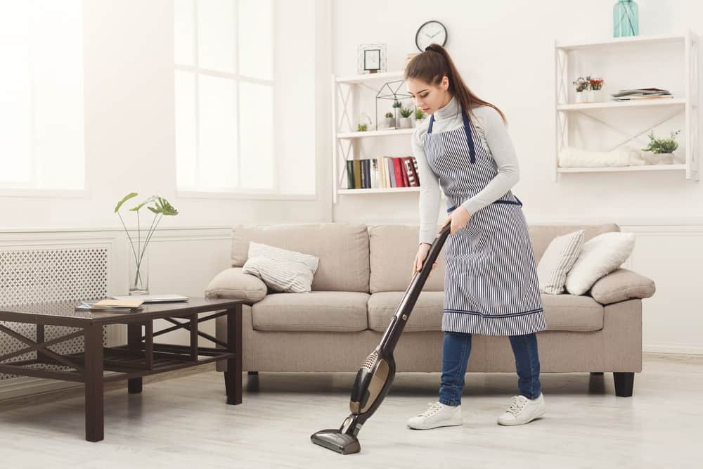 Woman cleaning the living room with stick vacuum cleaner