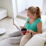 Woman drinking tea while robot vacuum cleans the floor