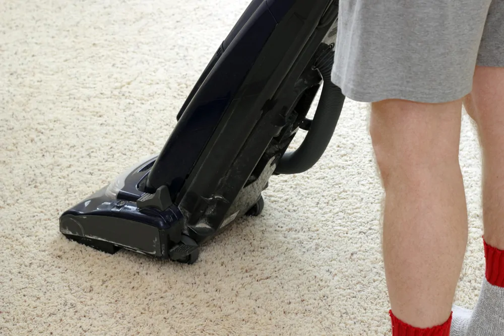 Man cleaning the carpet with an upright vacuum