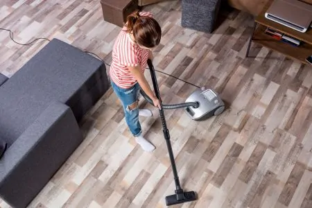 Young woman cleaning a laminate floor with a small vacuum