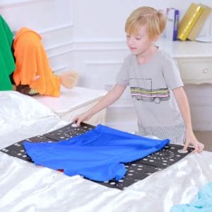 A young boy folding a shirt with a folding board