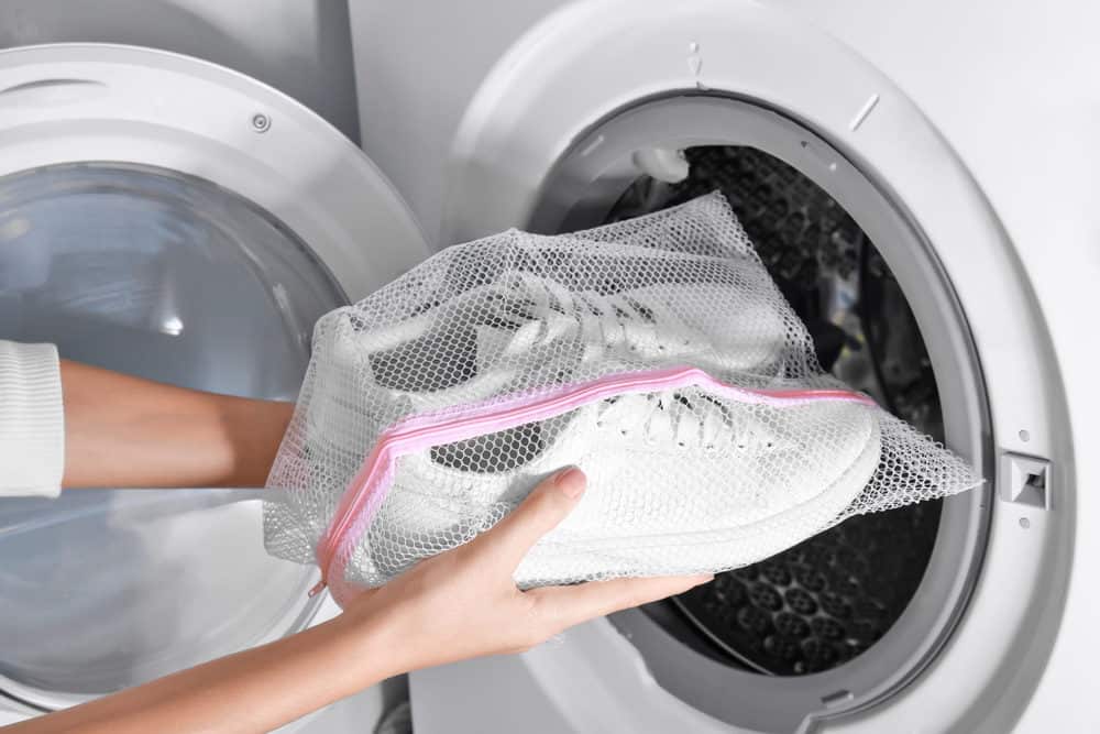 Woman putting mesh bag with white sneakers into washing machine