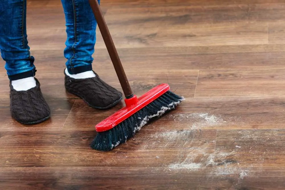 Cleaning woman sweeping wooden floor with push broom