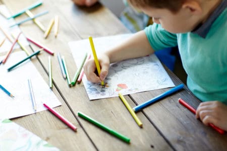 Little boy sitting and drawing with color crayons