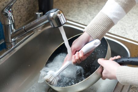 Woman scrubbing a dirty pan with dish scrubber