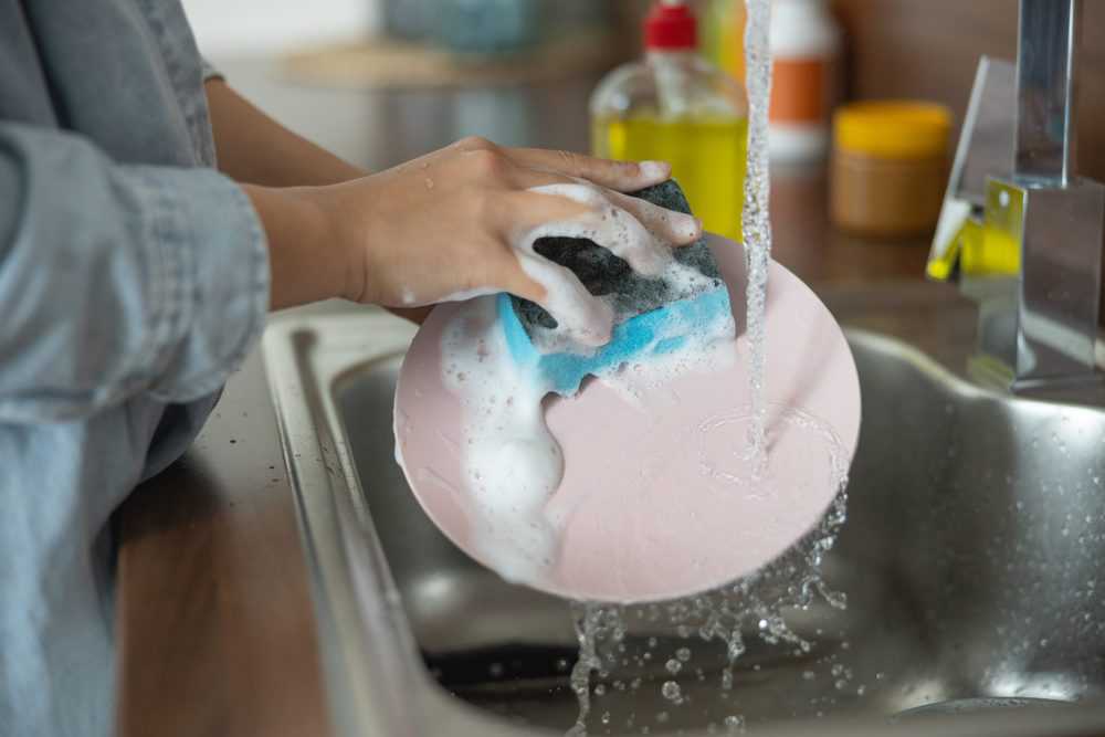 Woman washing a plate with liquid dish soap
