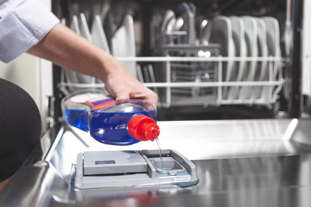 Woman filling dishwasher with liquid detergent
