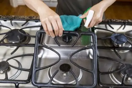 Hands cleaning stove top grates using a spray and cloth