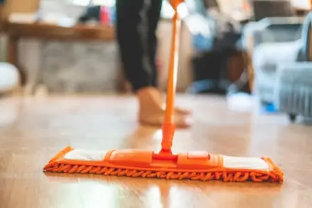 a person cleaning the vinyl floor using an orange mop