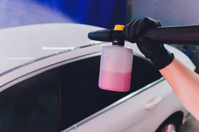 gloved hand cleaning the car using pressure washer with pink detergent