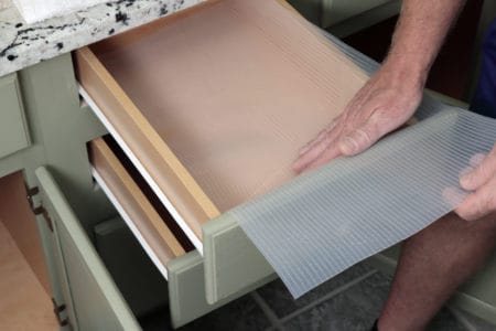 Man inserting a clear shelf liner into a bathroom drawer.