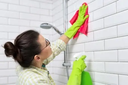 Woman cleaning shower tile wall