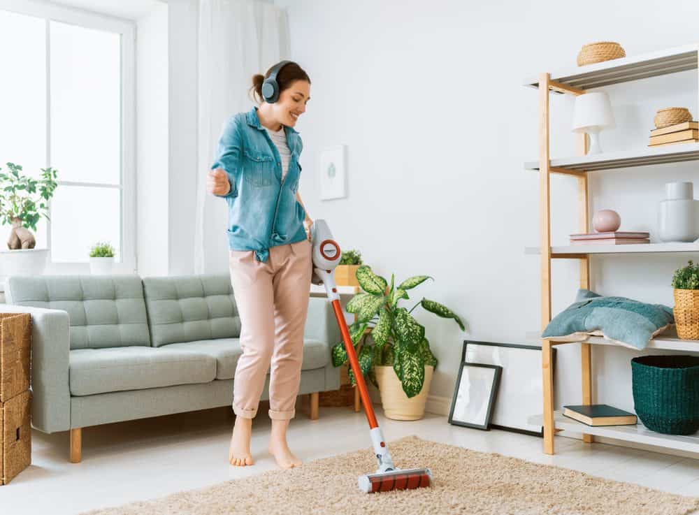 Beautiful young woman listening to music while cleaning the house with vacuum mop