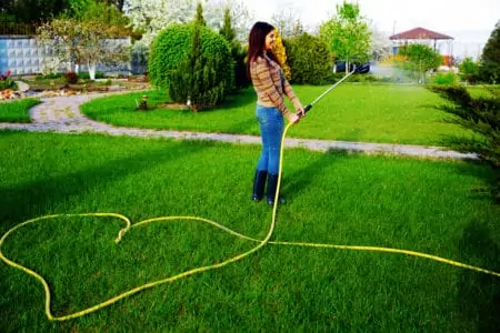 Woman watering grass with pressure washer hose