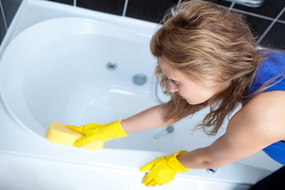 Young woman cleaning a stain off a bathtub