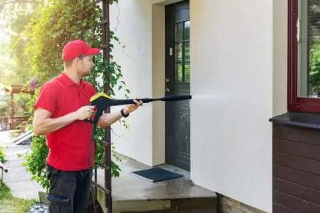 Man with high pressure washer cleaning house facade