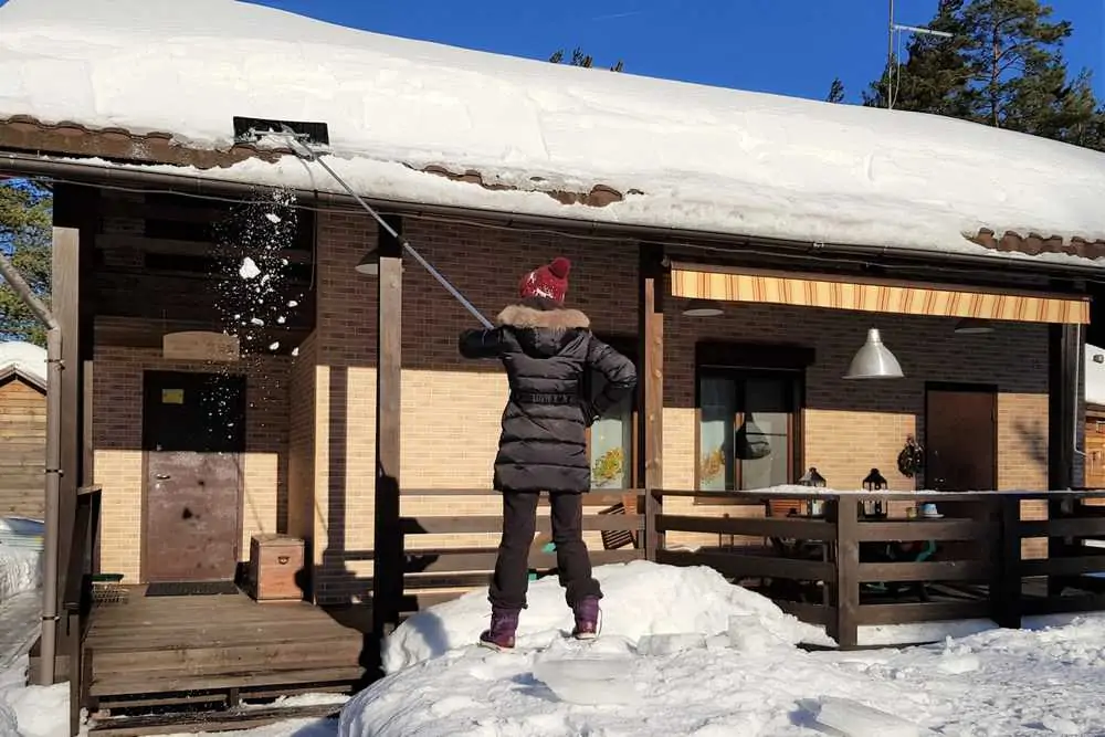 Woman cleans snow on the roof with rake