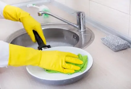 Woman wearing rubber gloves cleaning frying pan with cloth