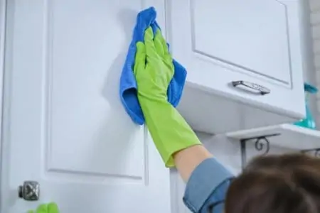 Woman in green gloves wiping kitchen cabinet using microfiber cloth