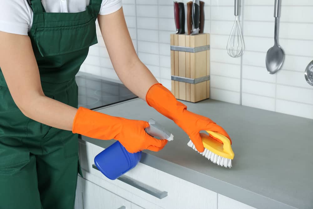 Woman cleaning kitchen slate countertop with spray and brush