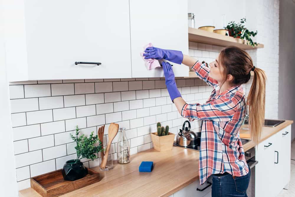 Woman wiping kitchen cabinets using cloth