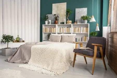 Tidy bedroom with a knit blanket on beige bed, between chair and tubes wall