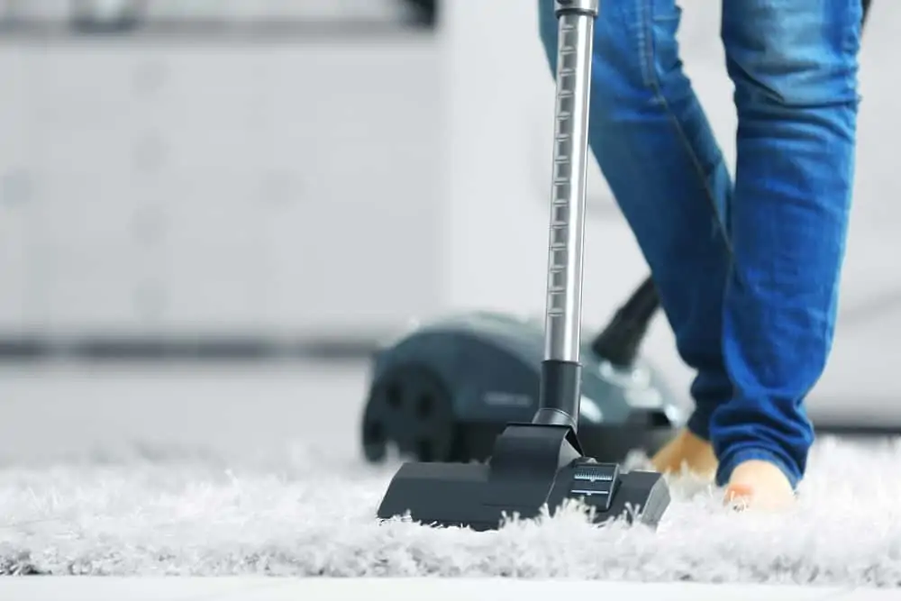 Woman cleaning the carpet with vacuum cleaner in the living room