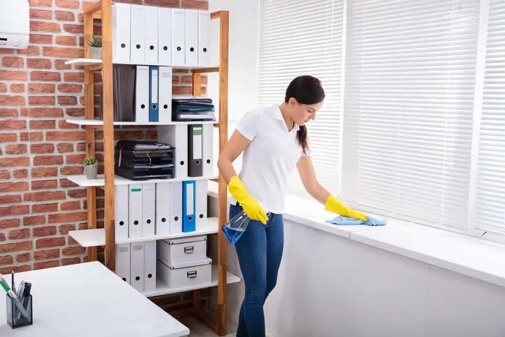 Woman cleaning window sill with spray bottle and napkin in the office