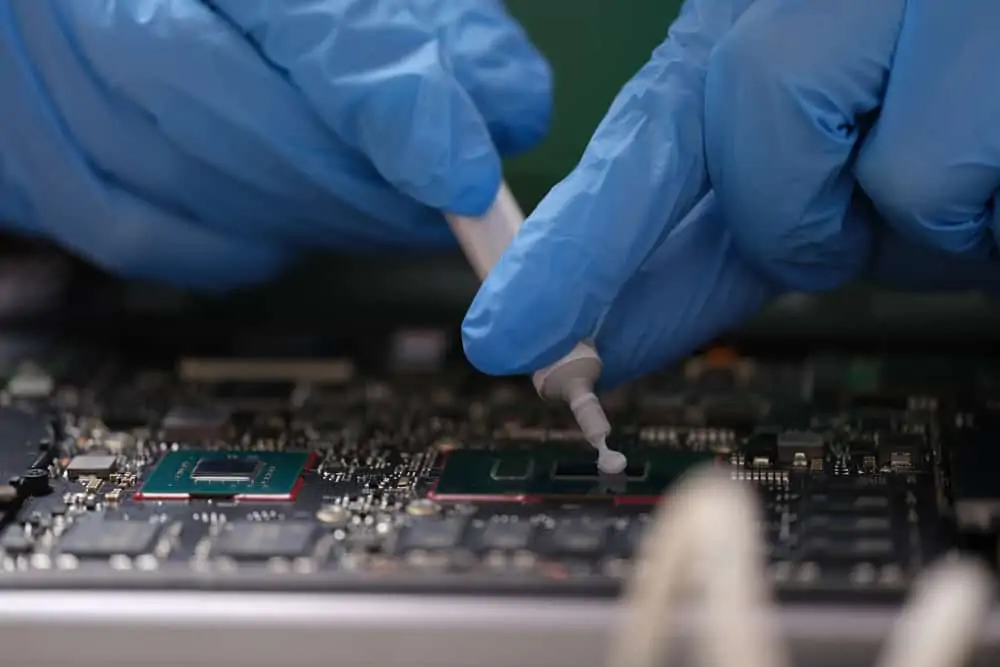 Gloved hands applying thermal paste on a laptop chip