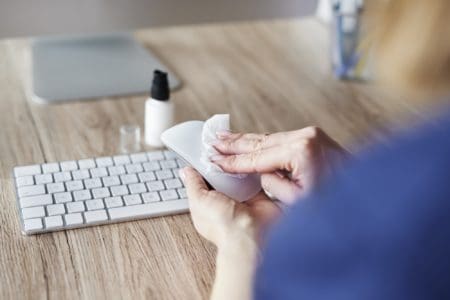 Woman wiping computer mouse with wipes