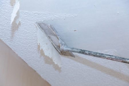 Removing popcorn ceiling at home with drywall scraper