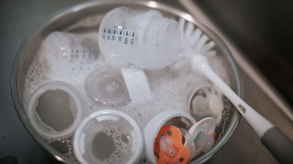 Washing baby bottles and nipples with soft bottle brush and dishwashing liquid