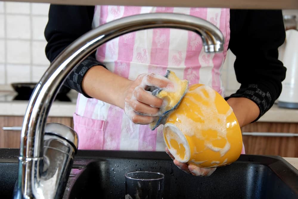 Woman washing dishes with sponge in kitchen sink 