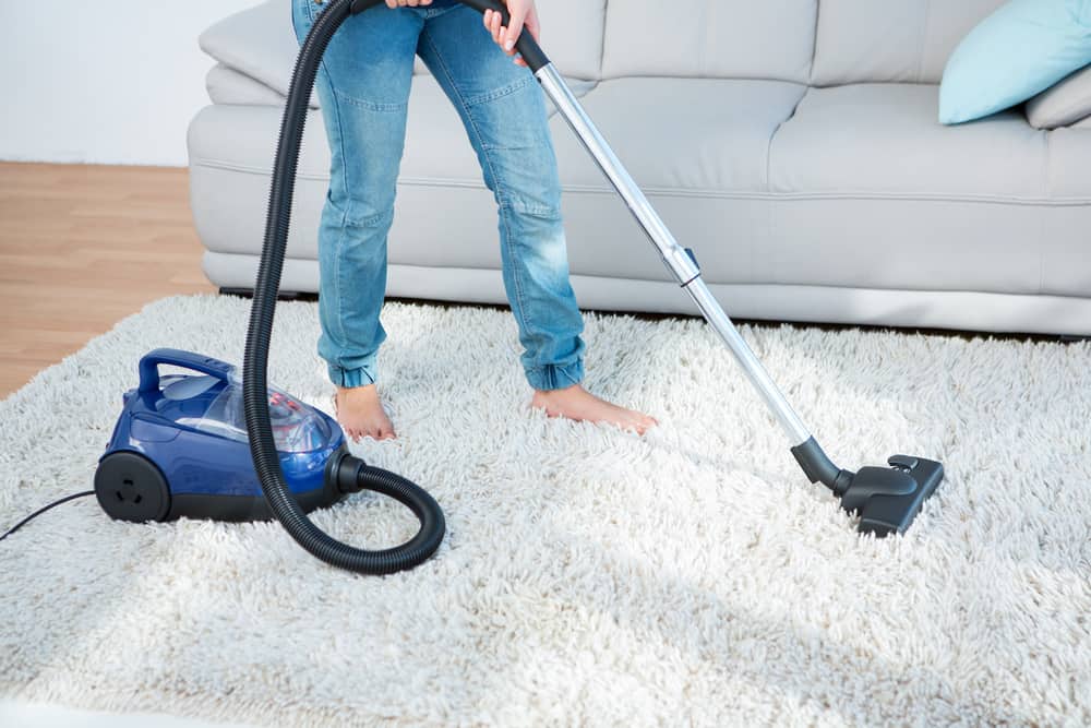 Woman using vacuum cleaner on shag rug at home in the living room