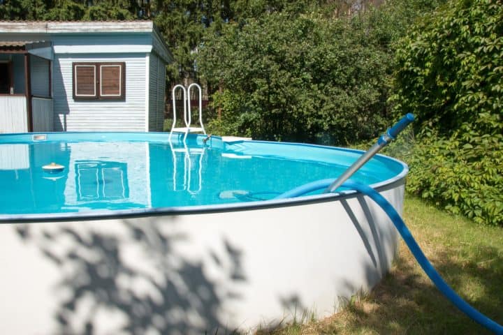 Vacuuming above ground pool on sunny backyard