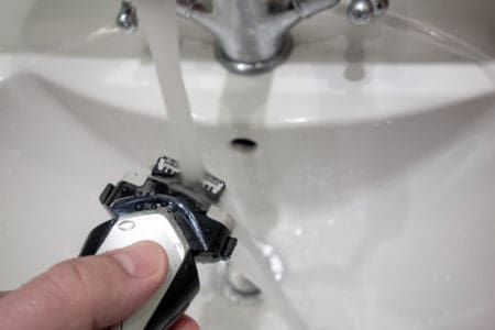 Person cleaning an electric razor using water faucet