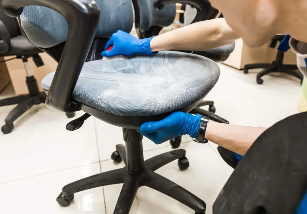 Man in rubber gloves cleaning fabric office chair with brush and soap
