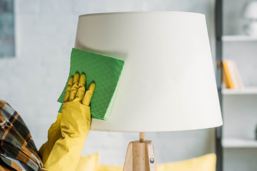 Cropped image of woman wiping lampshade with cloth
