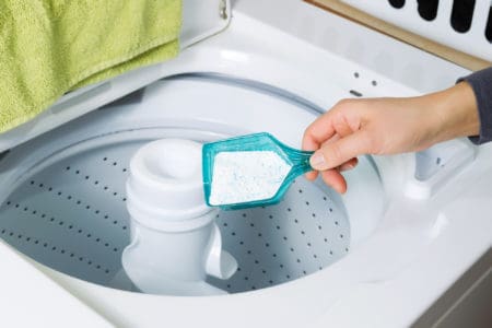 Cropped image of female hand putting in powdered soap into top load washer for laundry