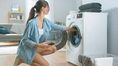 Woman sitting on knees loading washing machine with dirty clothes