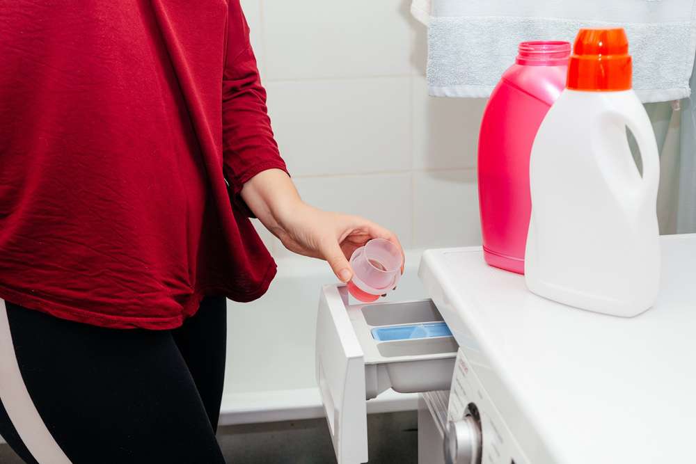 Woman pours liquid detergent into the washing machine tray