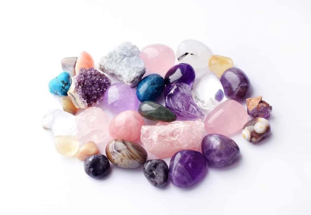 Collection of colorful gemstones including amethyst, rose quartz, and agate on a white background.