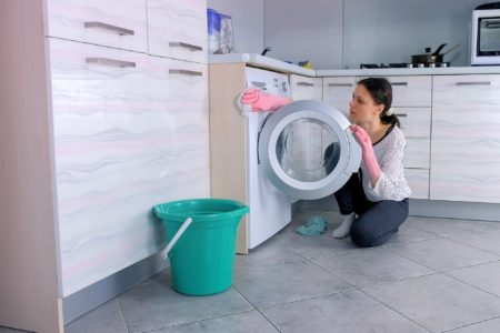 Woman wearing pink gloves cleaning front load washing machine