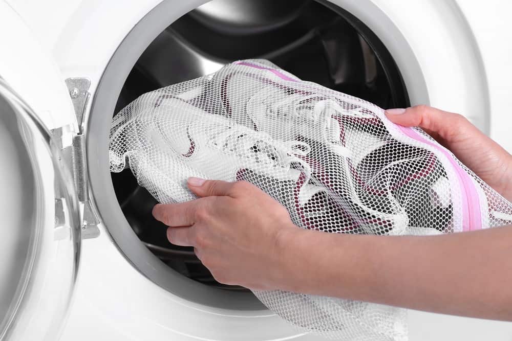 Woman putting pair of sneakers in mesh laundry bag into washer