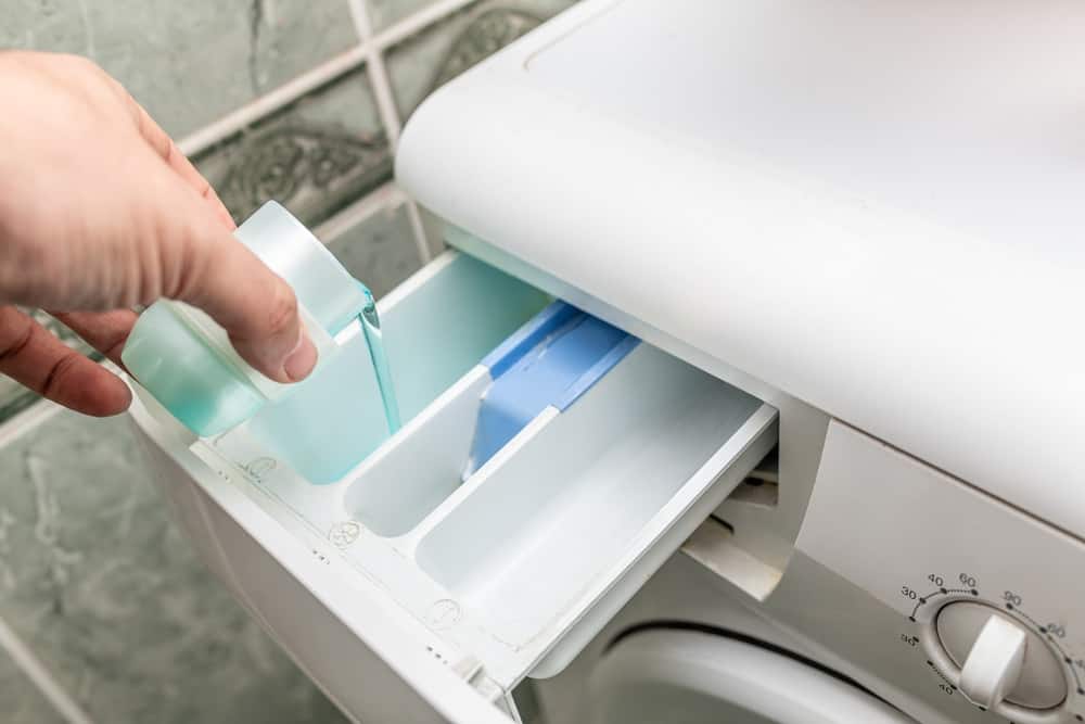 Male hand pouring laundry detergent into washing machine before doing the laundry