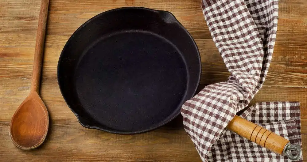 Cast iron skillet with wooden spoon and cloth on rustic table