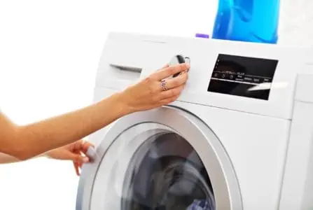 Woman setting cycle of front load washing machine with blue laundry detergent on top