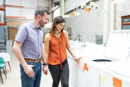 Happy couple holding hands while looking on white top load washer price tag at store